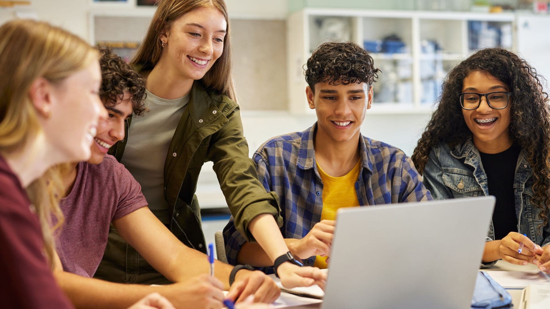 Students collaborating around a laptop in a bright lab classroom